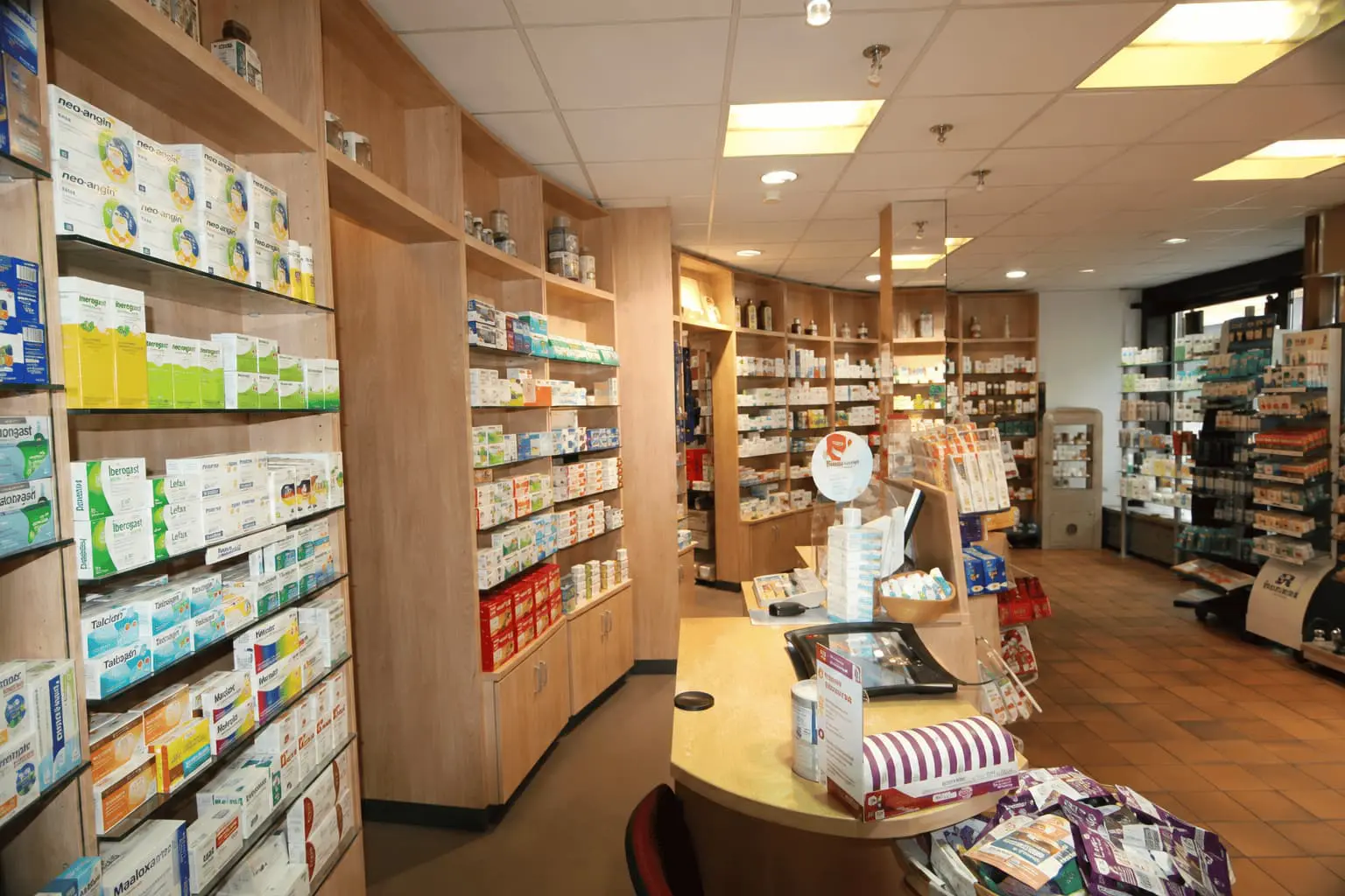 Helle Innenansicht einer Apotheke mit Medikamentenregalen, Verkaufsbereich und übersichtlich präsentierten Gesundheitsprodukten.